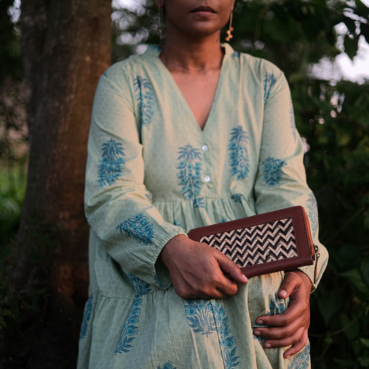 Woman in a light green dress with blue patterns holding a brown clutch with a zigzag pattern.