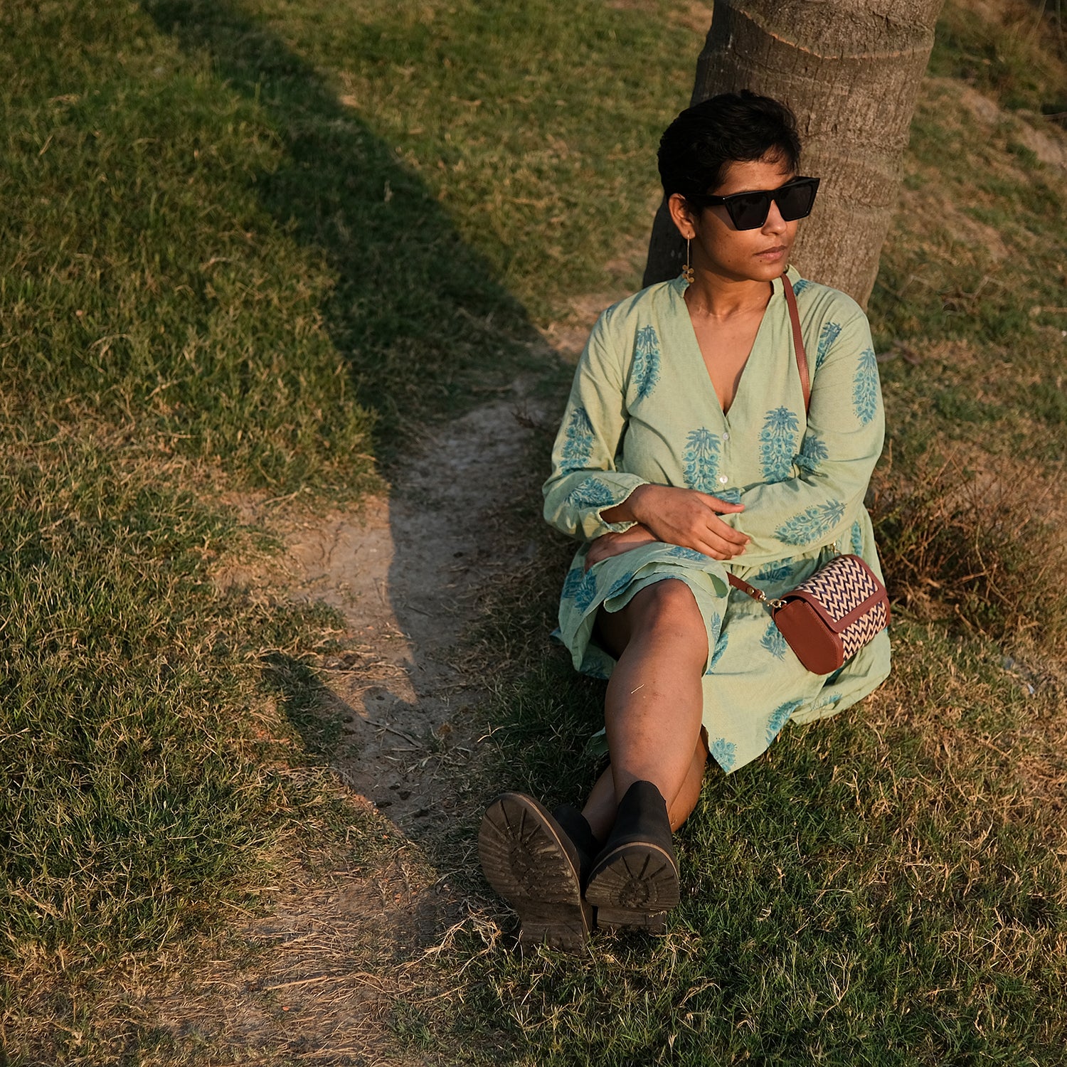 Woman in a light green dress sitting on grass next to a tree
