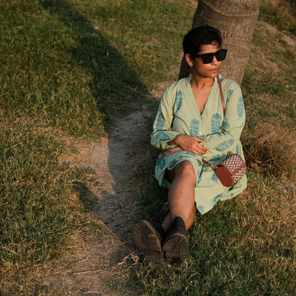 Woman in a light green dress sitting on grass next to a tree
