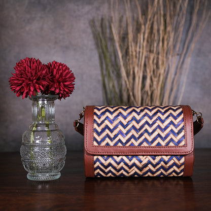 Woven handbag with zigzag pattern next to a vase with red flowers on a wooden surface.