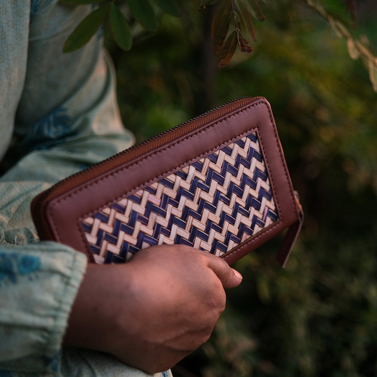 Hand holding a brown wallet with a patterned interior against a blurred natural background