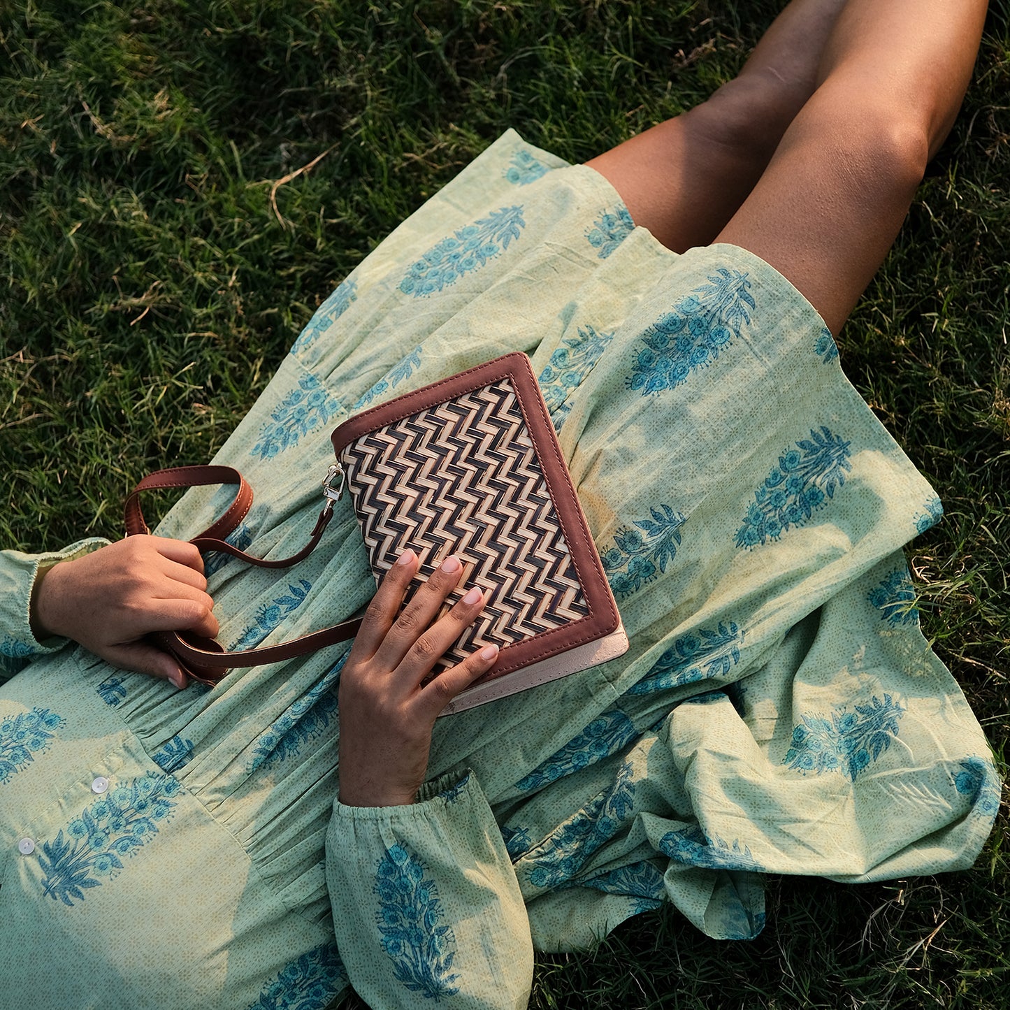 Person sitting on grass holding a patterned bag