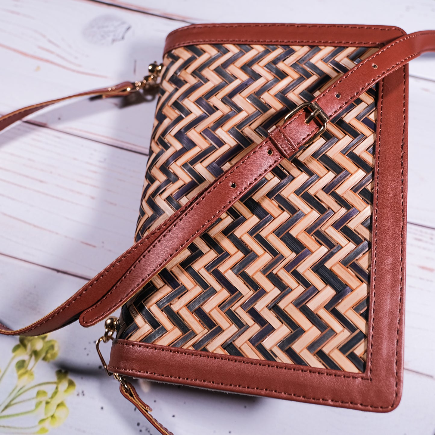 Woven handbag with brown leather accents on a light wooden surface