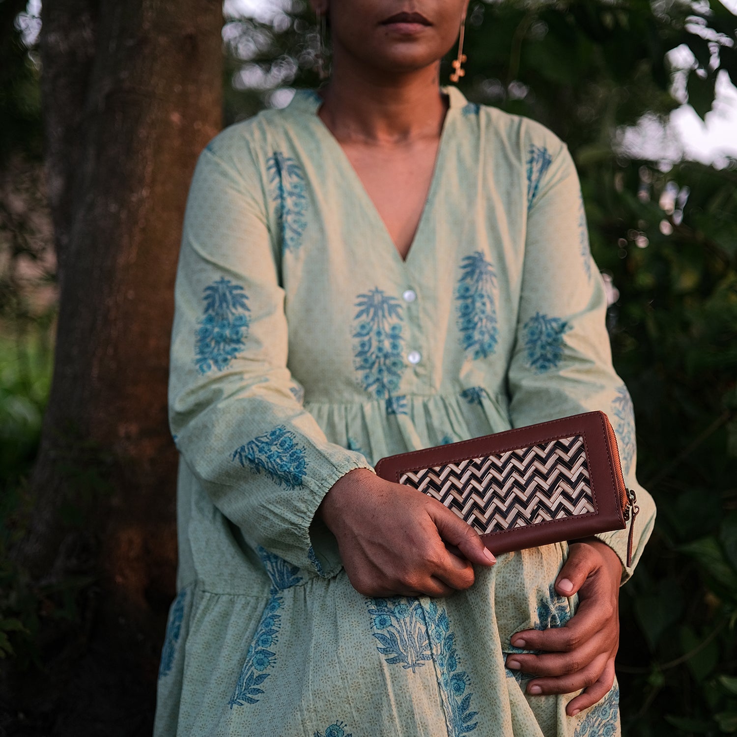 Woman in a light green dress with blue patterns holding a brown clutch with a zigzag pattern.