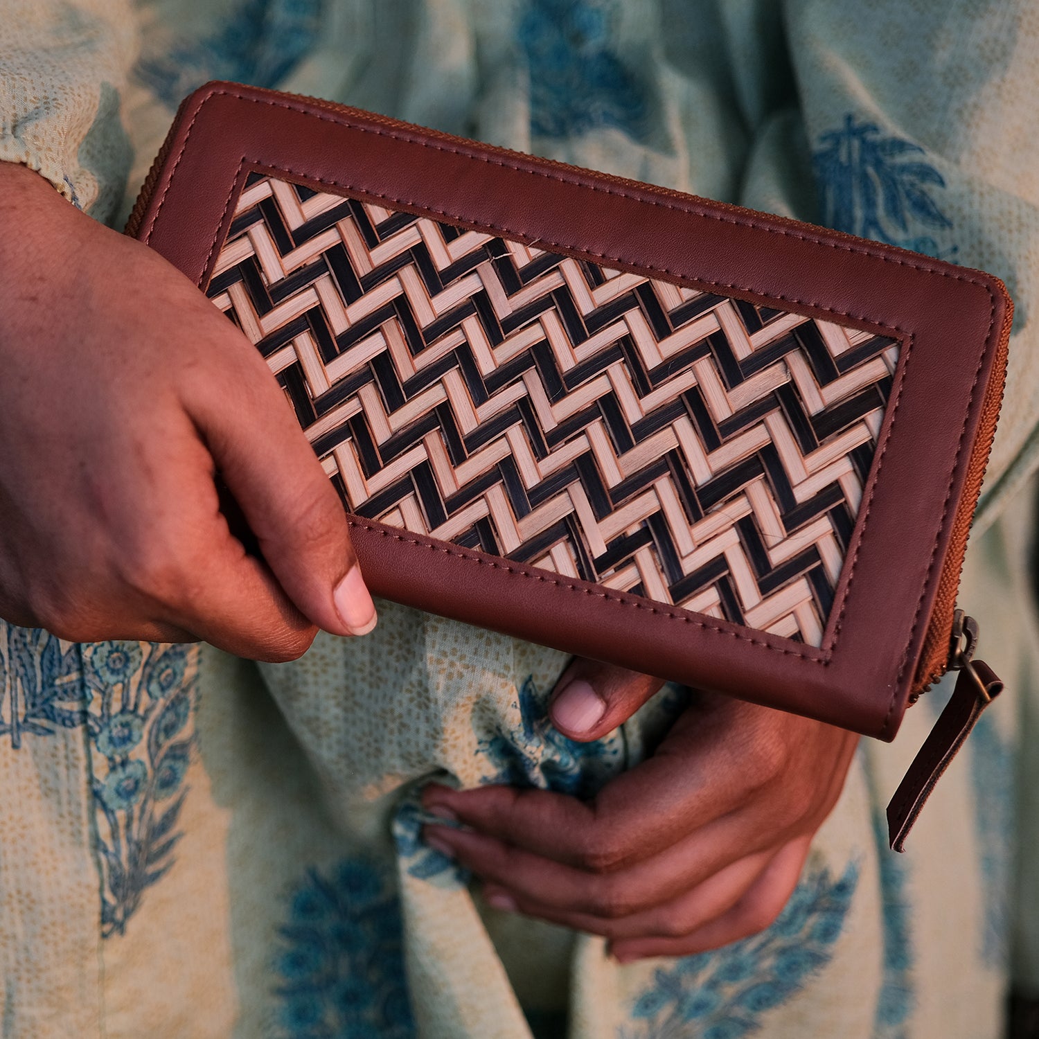 Brown wallet with a geometric pattern held by a person against a patterned fabric background